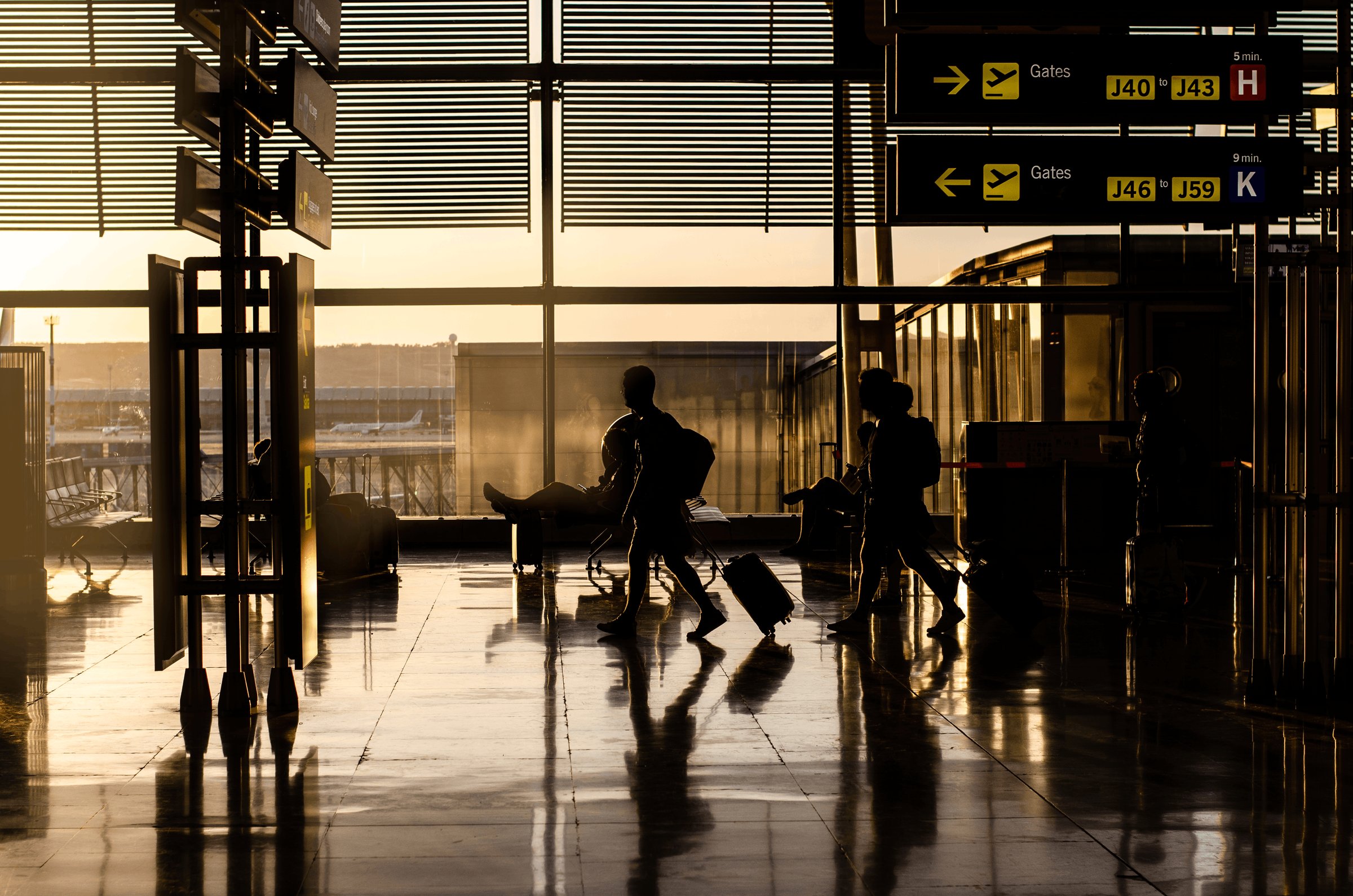 Travellers walking through an airport terminal at sunset, gate signs above
